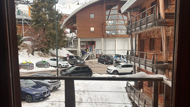 A wooden deck with a view of a snowy parking area, a building with a wooden facade, and a large tree. - Duplex Apartment for 4 at Les Balcons Du Recoin with Balcony (Chamrousse)