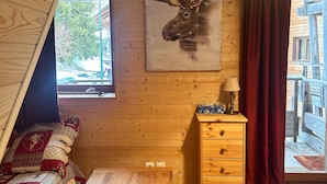 A cozy cabin interior with a wooden wall, a painting of a moose head, a wooden dresser, a table, and a window with a view of the outside. - Duplex Apartment for 4 at Les Balcons Du Recoin with Balcony (Chamrousse)