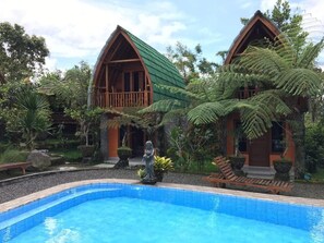 A resort with two wooden cabins, a swimming pool, and lush greenery. - Sandan Agro Resort (Kintamani)