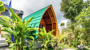 Een huis met een groen dak en houten wanden, omgeven door weelderig groen en een stenen pad.