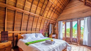 Een slaapkamer in een houten hut met een groot bed, houten wanden en een balkon met uitzicht op groen.