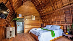 Een houten kamer met een bed, een klein tafeltje, een wastafel en een televisie.
