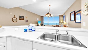 Una cocina moderna con una isla grande, pileta de acero inoxidable y vista al mar a través de amplios ventanales.