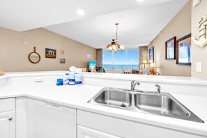 A modern kitchen with a large island, stainless steel sink, and a view of the sea through large windows. - ☀️Amazing Views | Beach Front | XL Balcony | Majestic Beach Towers 2-2107☀️ (Panama City Beach)