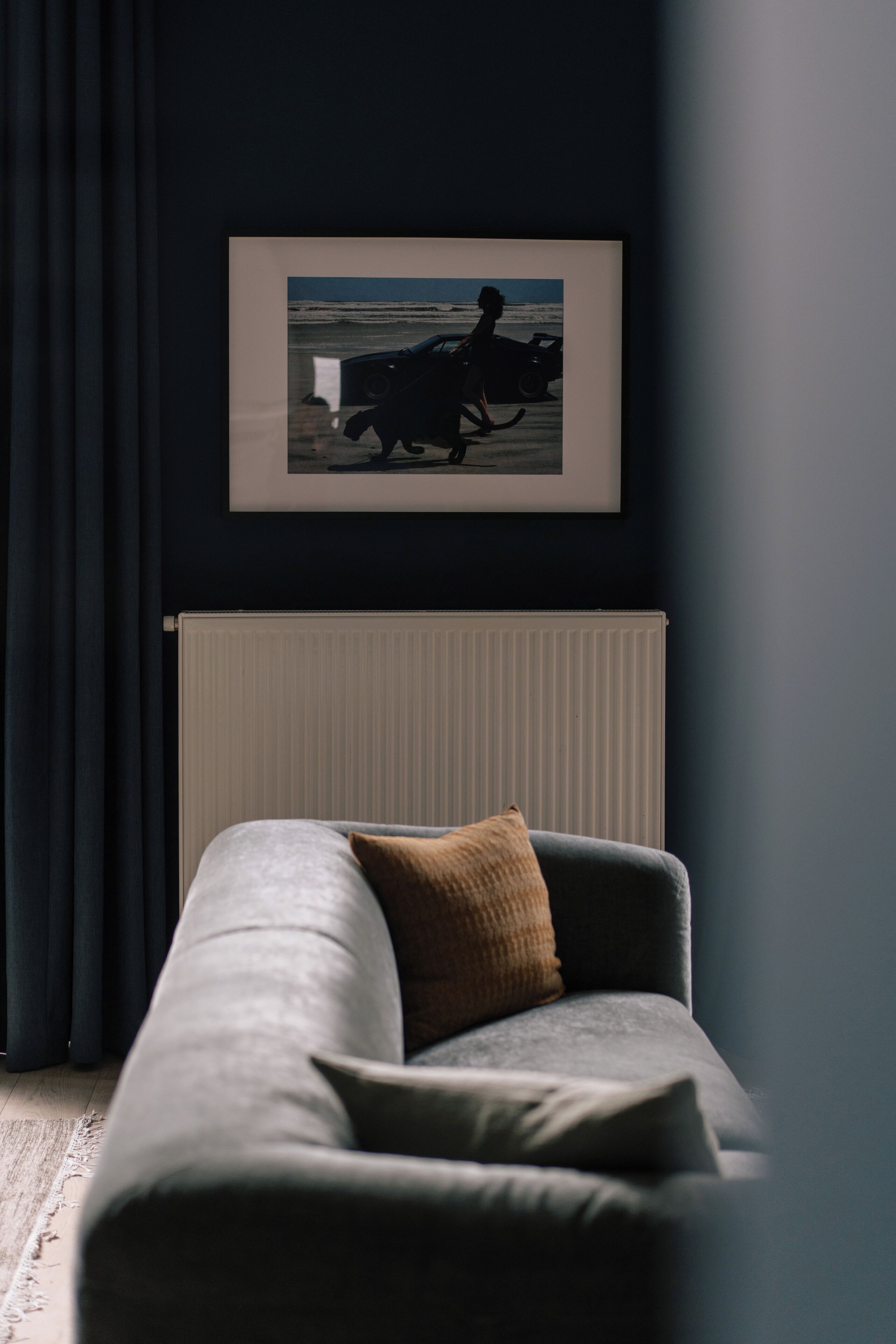 A modern living room with a grey sofa, a framed picture on the wall, and a radiator below.