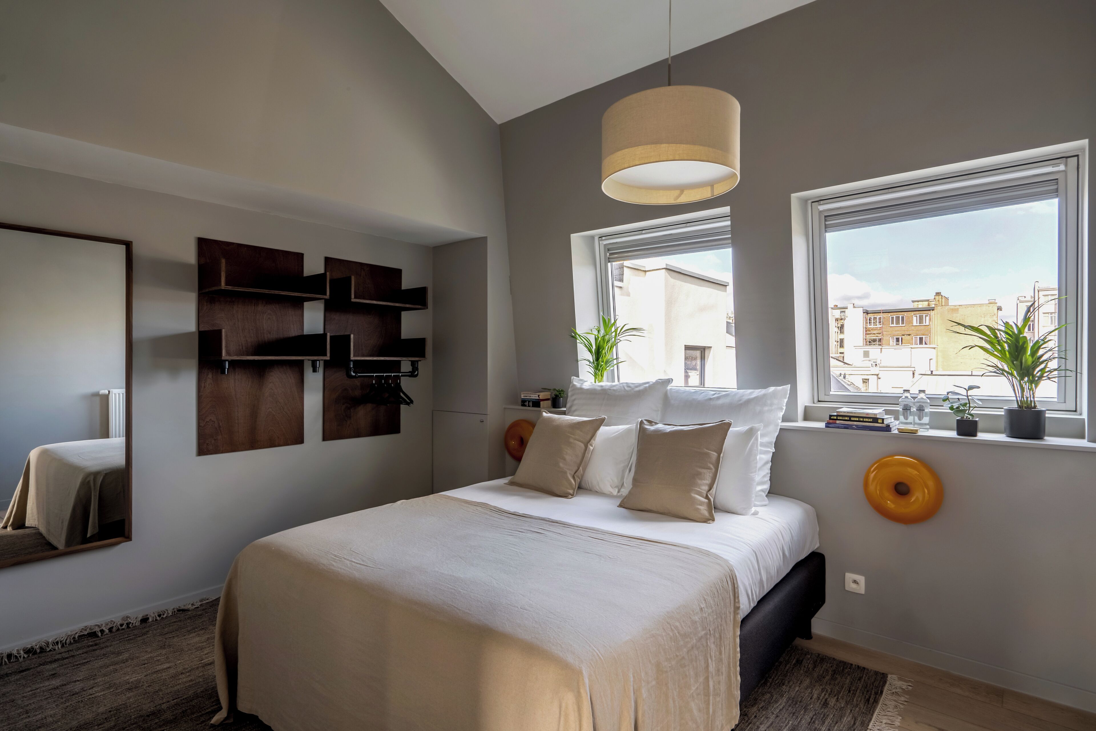 Un dormitorio moderno con una cama grande, una estantería en la pared, un ventanal con vistas y una lámpara colgante.