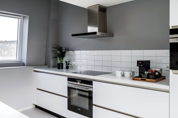 A modern kitchen with white cabinetry, a stainless steel range hood, a built-in oven, and a coffee maker on the countertop. - A Place - Schuttershofstraat 5 (Antwerp)