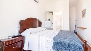 A bedroom with a wooden bed, a bedside table, a wardrobe, and a door leading to another room. - VCGuesthouse Neto's Room (Funchal)