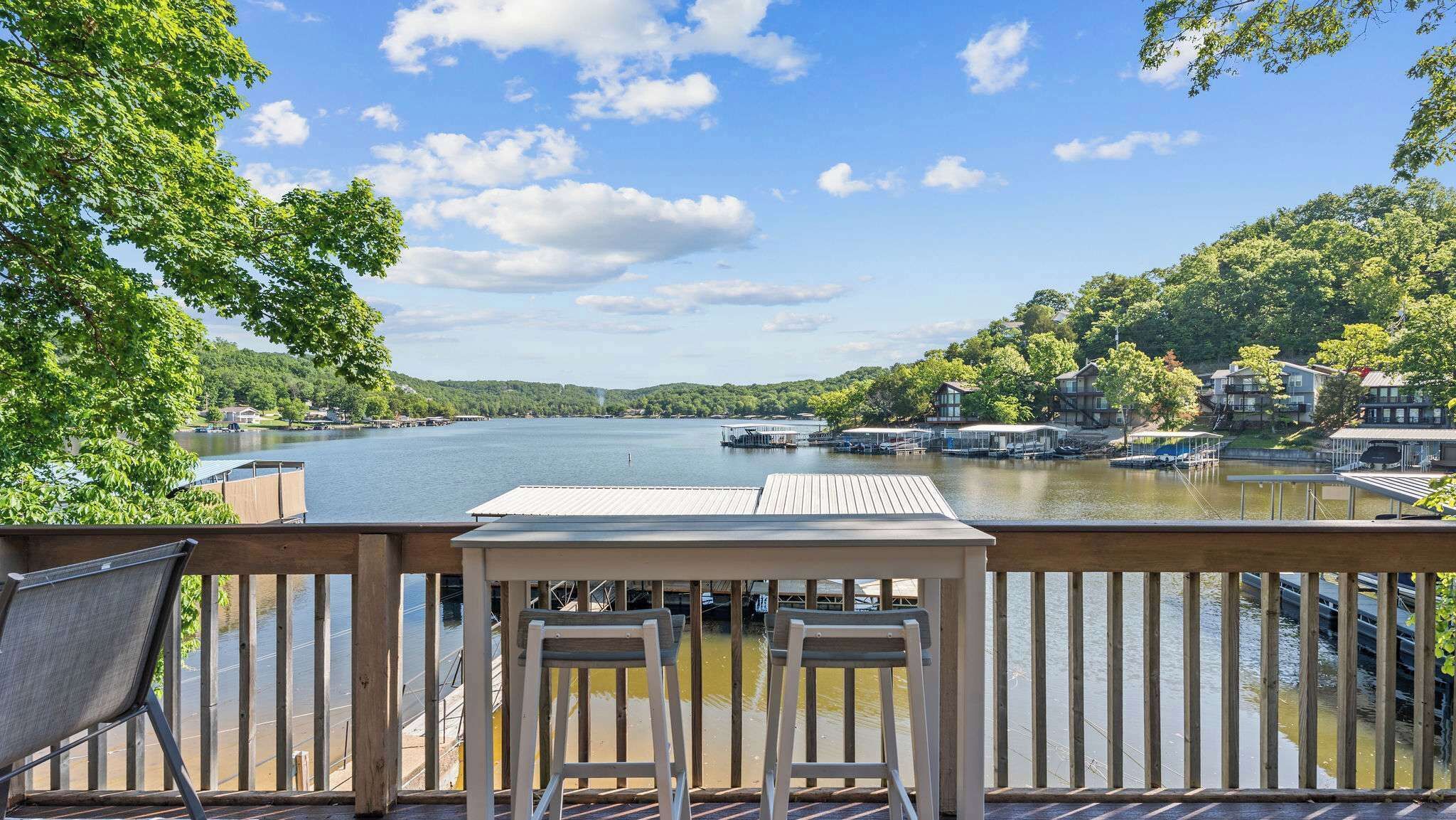 A lakeside view from a deck with a table and chairs, docked boats, and houses in the background.