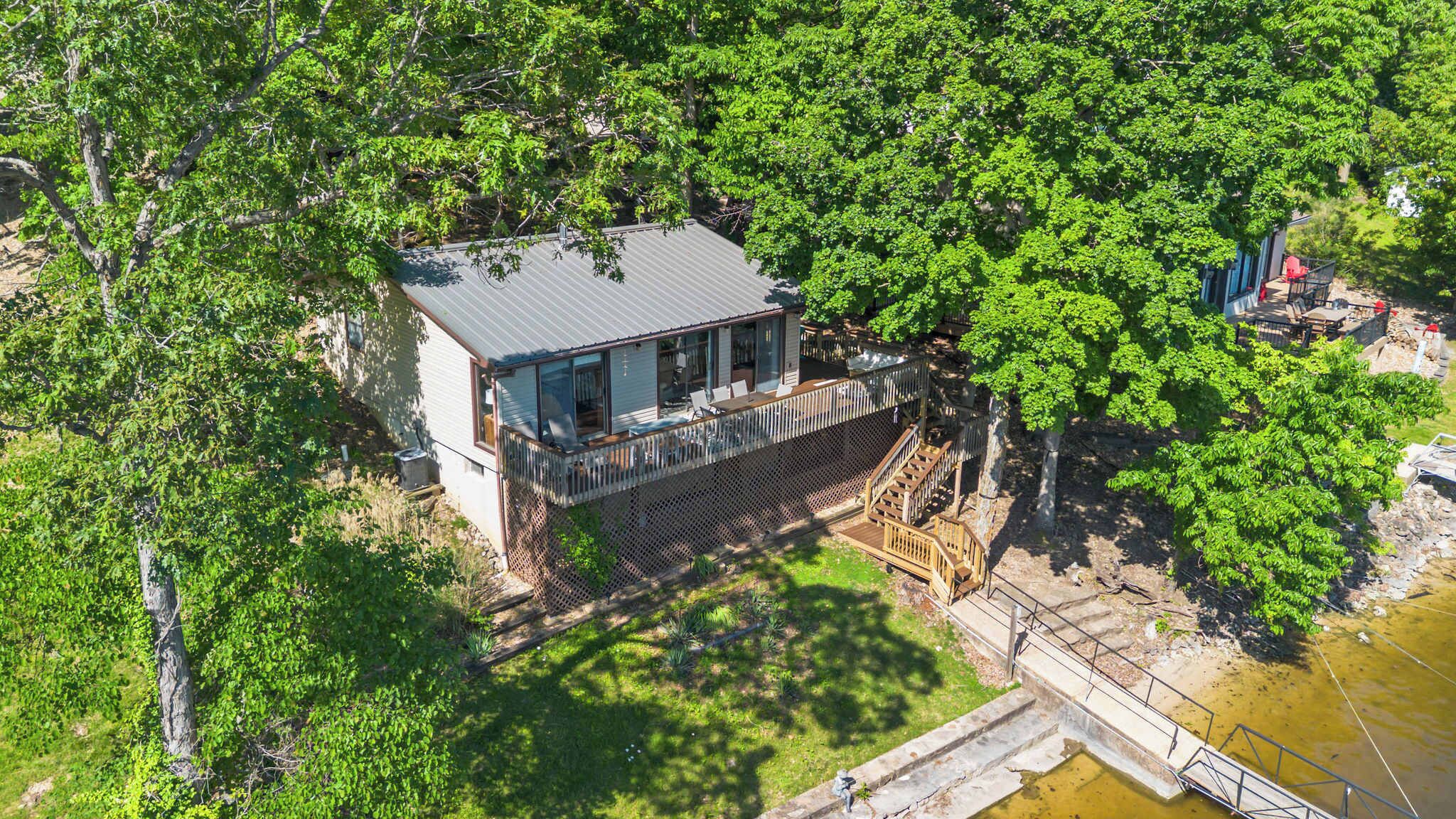 A house with a deck, surrounded by trees, near a body of water.