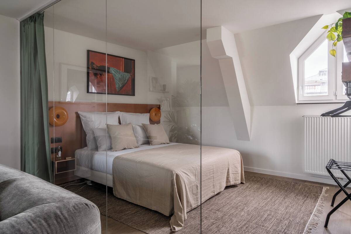 Un dormitorio con cama, mesita de noche, lámpara, ventana con planta y radiador.