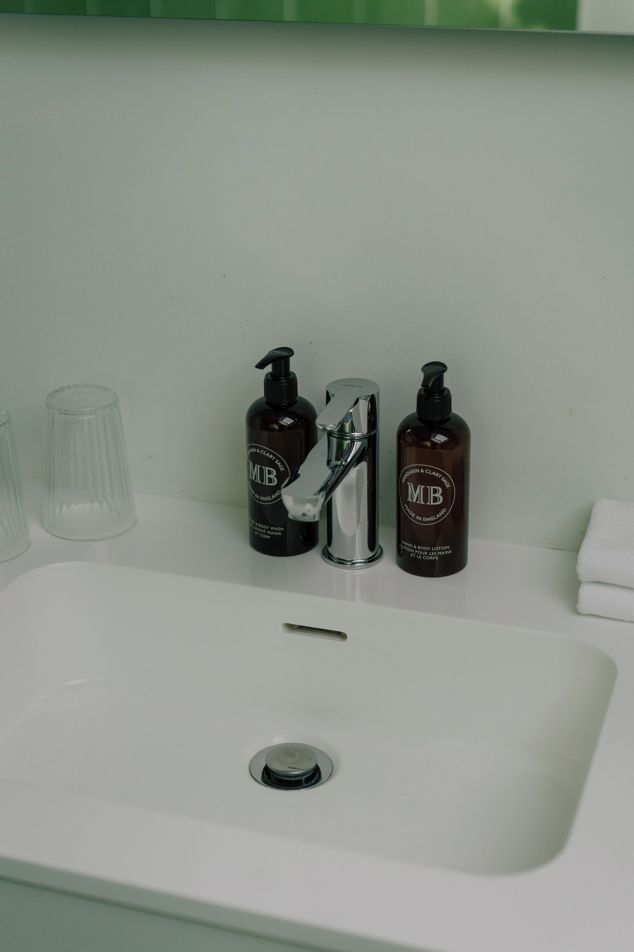 Un lavabo de salle de bain avec deux flacons de lotion pour le corps de la marque MJB, un verre transparent et une serviette blanche.