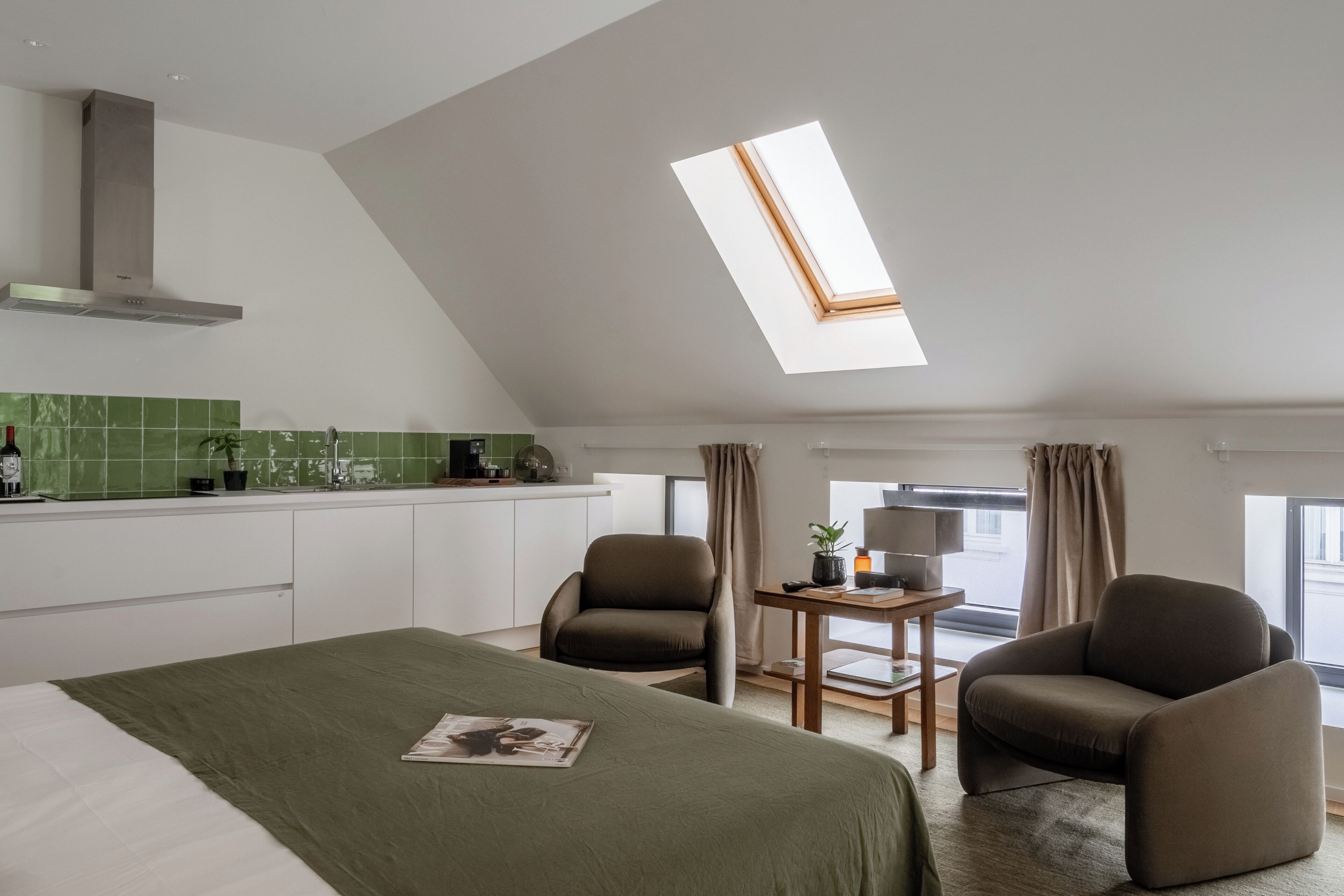 Een moderne hotelkamer met dakraam, een bed, twee fauteuils, een tafeltje en een kitchenette.