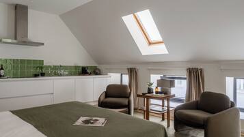Een moderne hotelkamer met dakraam, een bed, twee fauteuils, een tafeltje en een kitchenette.