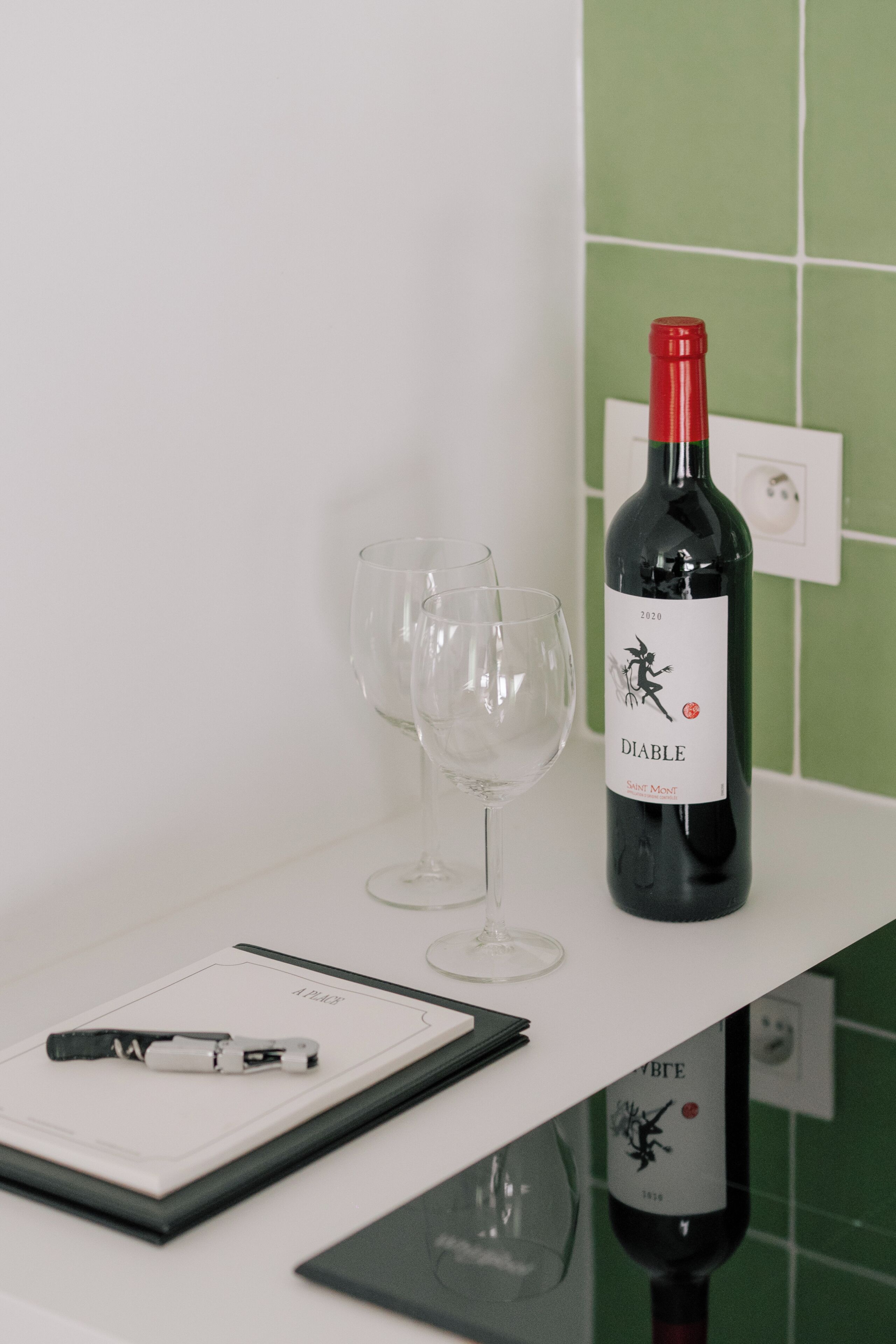 Een fles wijn met de aanduiding 'Diable Saint Mont' op een witte ondergrond, met twee lege wijnglazen en een klembord.