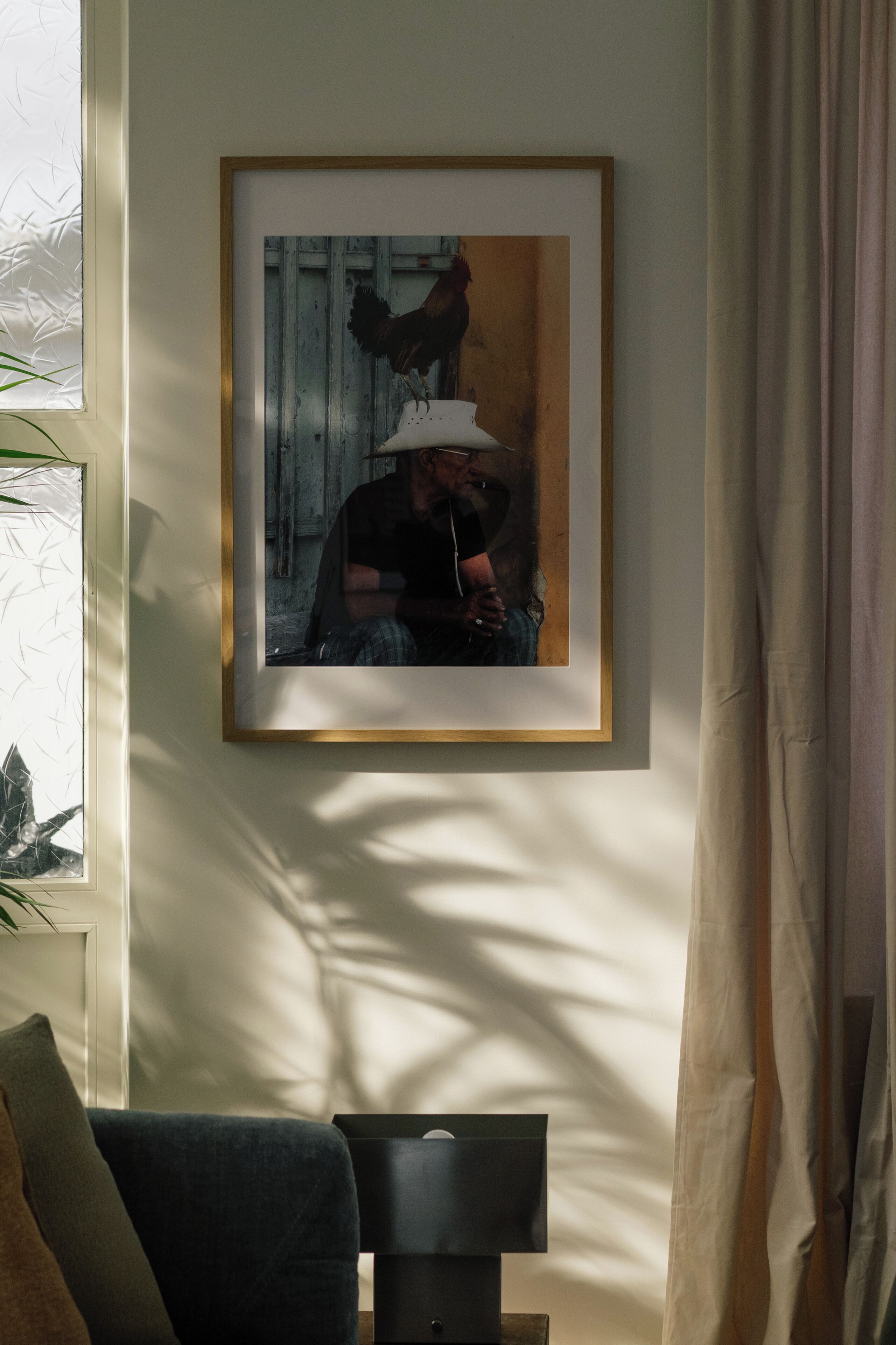 A framed picture on a wall, a window with blinds, and a lamp on a table.