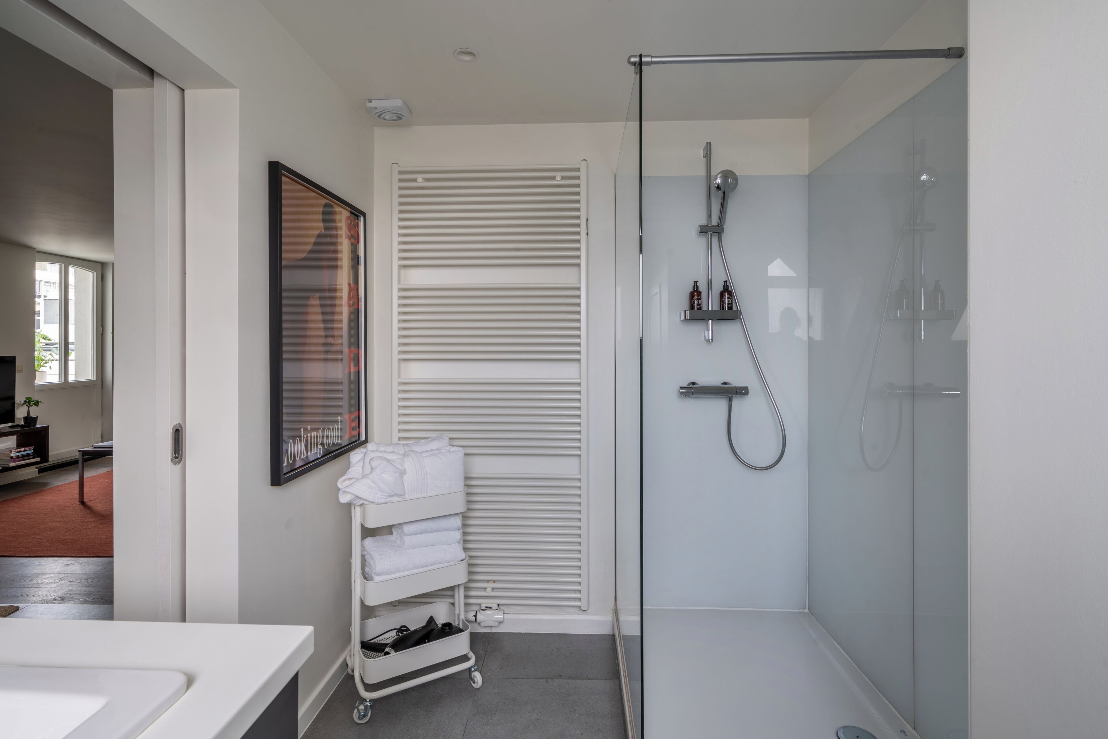 A modern bathroom with a glass shower enclosure, a white towel rack, and a framed artwork on the wall.