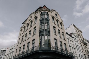 Un edificio en esquina con un balcón curvo, ventanas amplias y detalles de hierro ornamentados.
