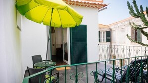 Un balcon avec un parasol vert, des chaises en osier et une table.