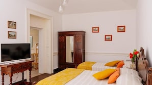 Une chambre d’hôtel avec deux lits, un téléviseur posé sur une table en bois, une armoire et des tableaux encadrés accrochés au mur.