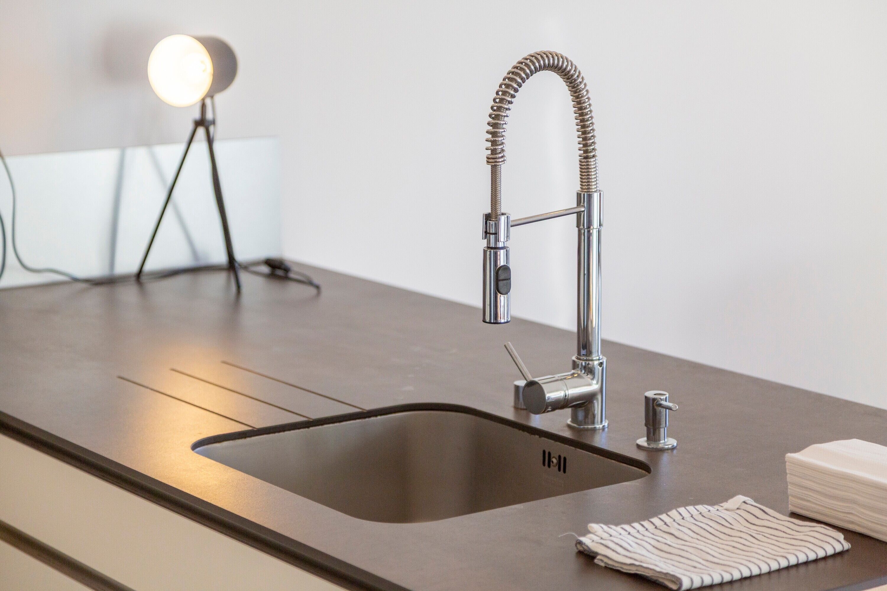 A modern kitchen with a stainless steel sink, a flexible faucet, and a round light on a tripod.