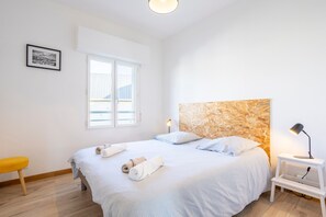 A bedroom with a bed, a bedside table with a lamp, a window, and a framed picture on the wall. - L'Urania – Stay in the Heart of Concarneau (Concarneau)
