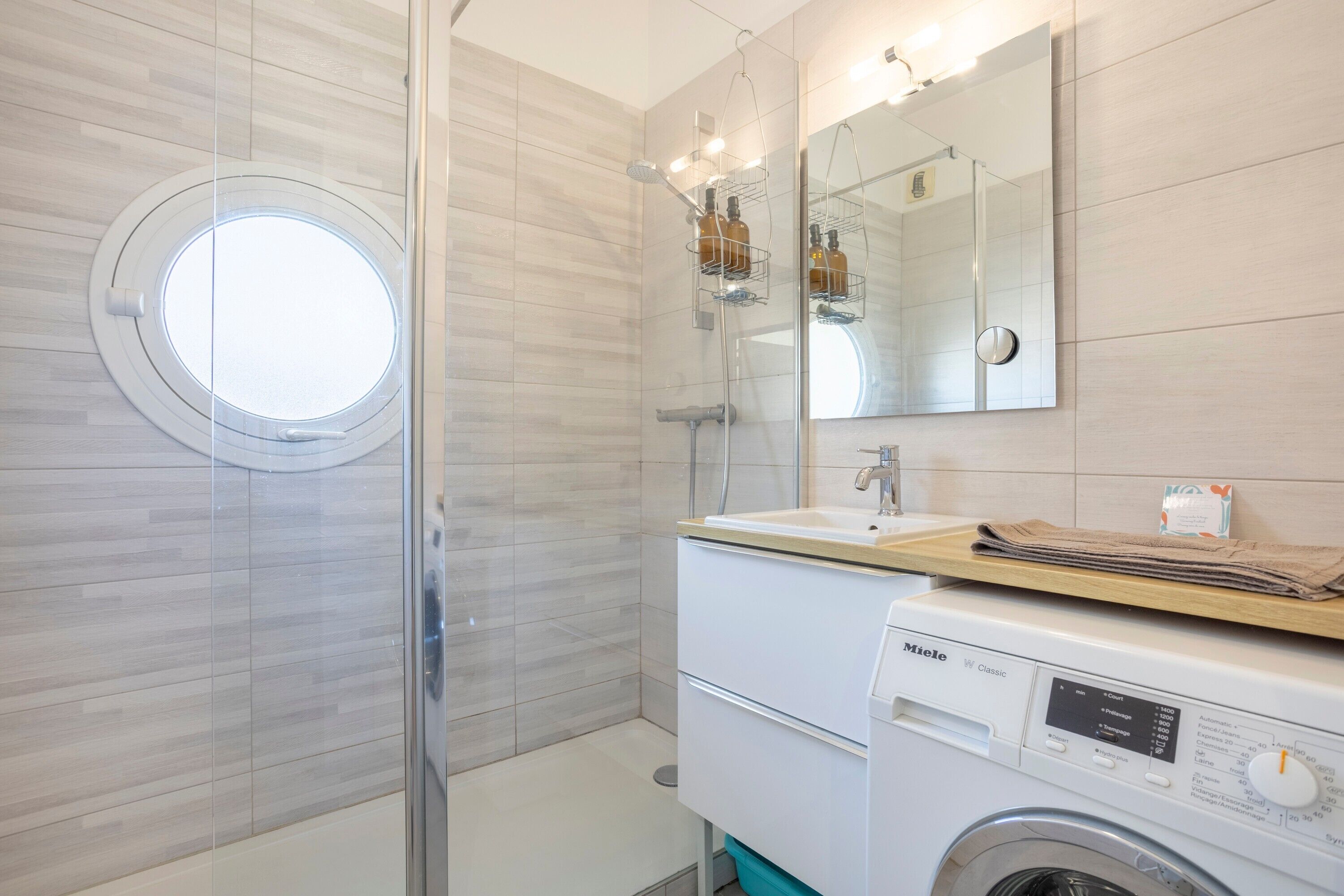Een moderne badkamer met een glazen douchecabine, een rond dakraam, een inbouw wastafel en een wasmachine.