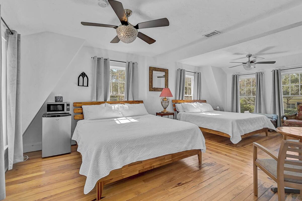 A bedroom with two beds, a ceiling fan, a microwave, and a small table.