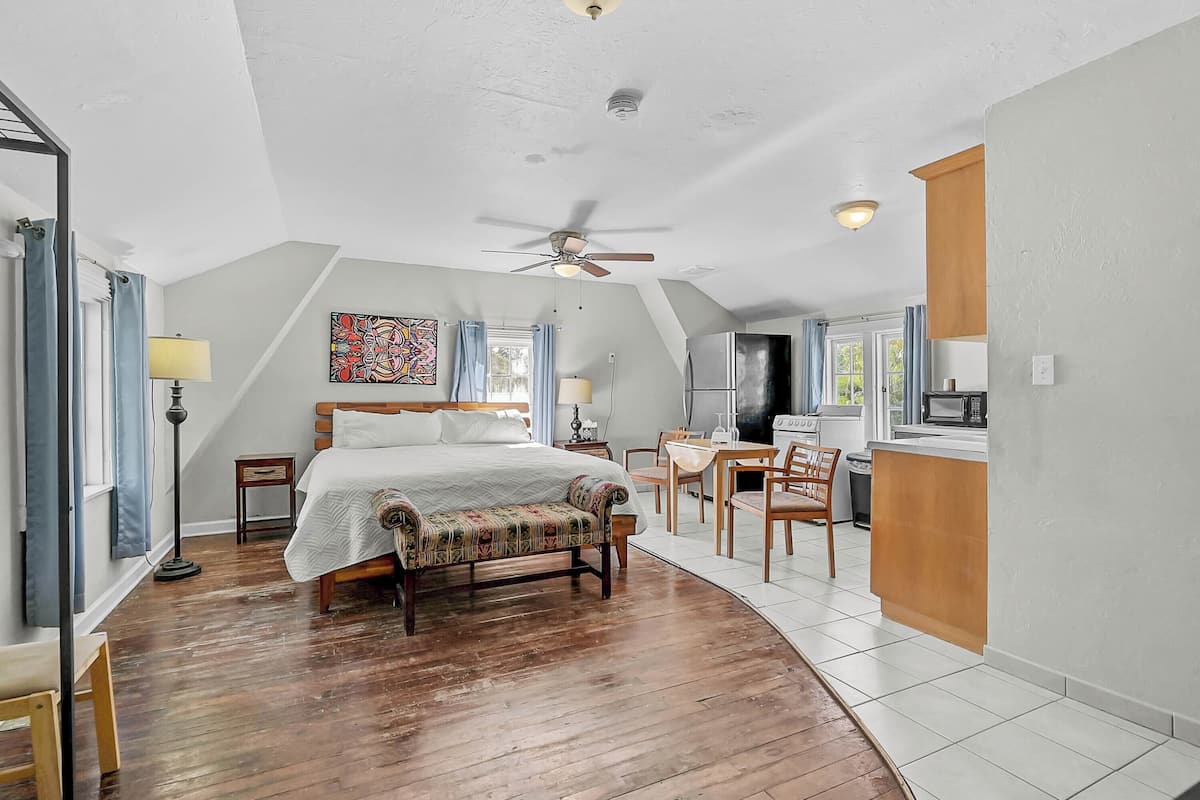 A bedroom with a bed, a desk, and a kitchenette.