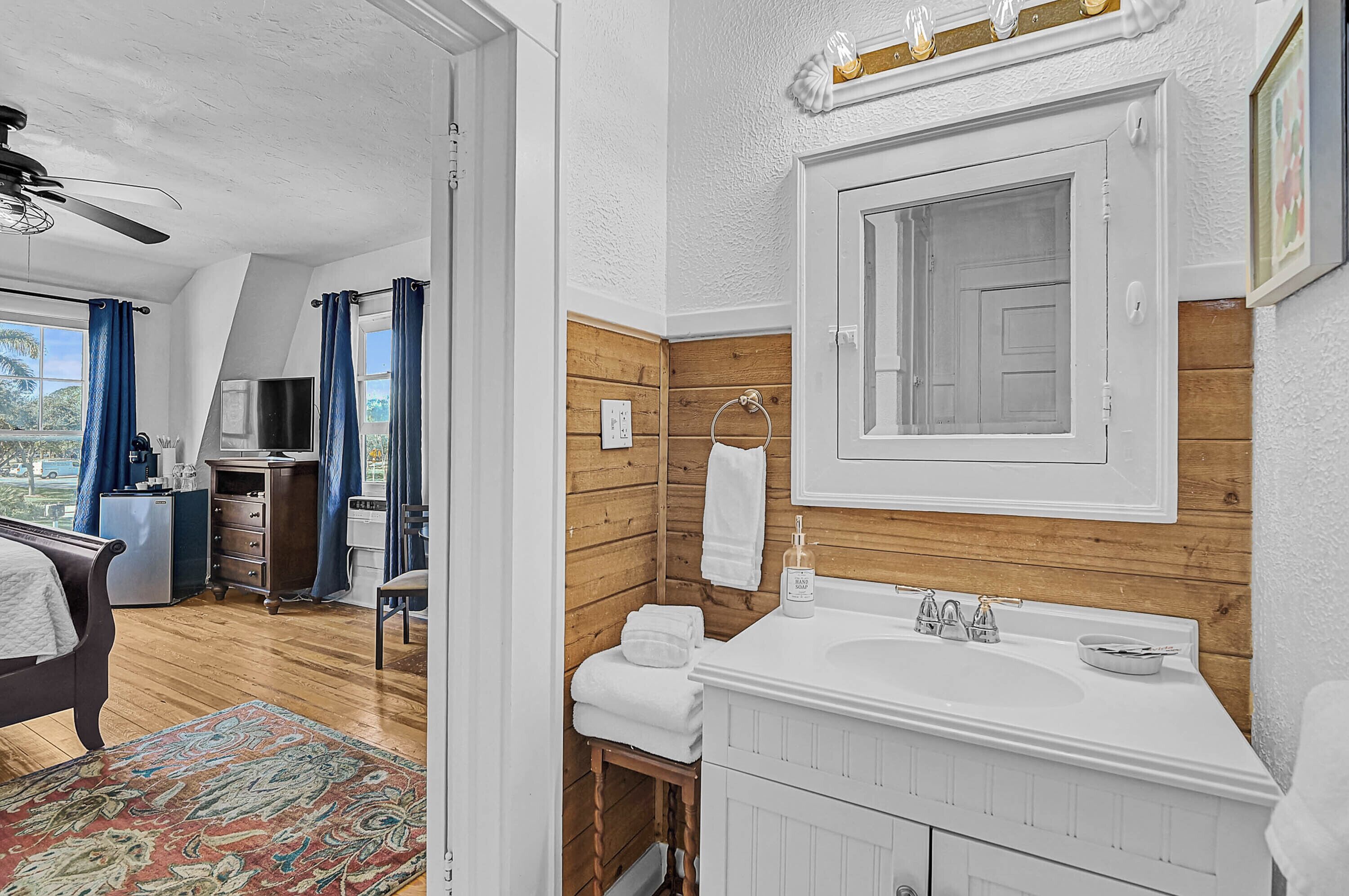 A modern bathroom with a wooden accent wall, a white sink, and a large mirror.