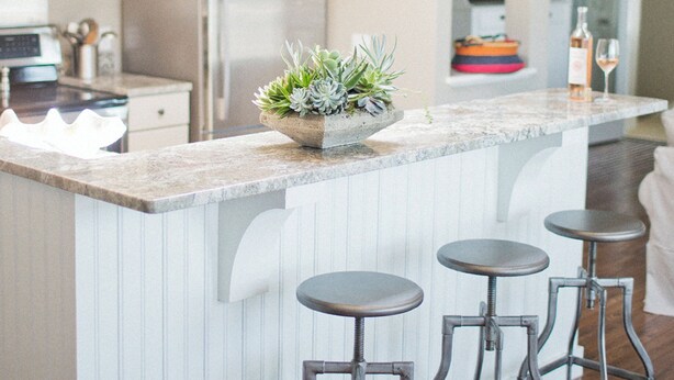 Une cuisine moderne dotée d’un îlot central, de tabourets de bar, d’appareils électroménagers en acier inoxydable et de luminaires suspendus.
