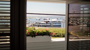 Une vue d’une marina où plusieurs bateaux sont amarrés, avec un ciel dégagé et, au loin, une rue bordée de voitures et d’immeubles.