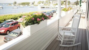 Une terrasse en bois avec une chaise berçante blanche, une rangée de plantes en pot et une vue sur les bateaux qui naviguent.