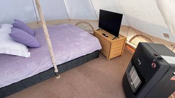 A compact room with a bed, a television on a wooden stand, and a portable heater.