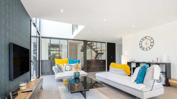 A modern living room with a sofa, coffee table, TV, and a clock on the wall. - Exceptional Villa with Garden – 10 Minutes from Combrit Beaches (Combrit)