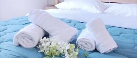A neatly made bed with blue bedding, white pillows, and rolled white towels.