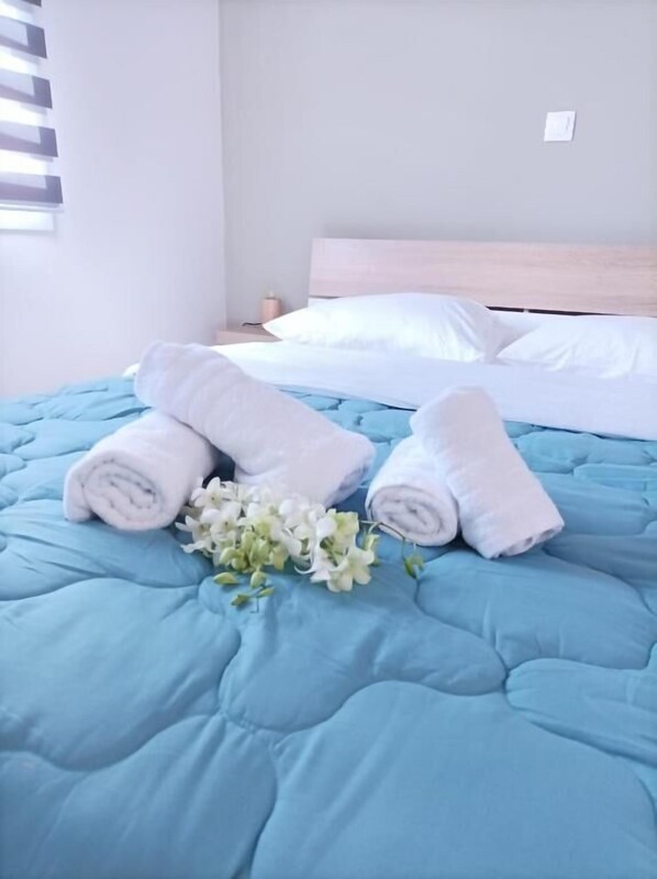 A neatly made bed with blue bedding, white pillows, and rolled white towels.