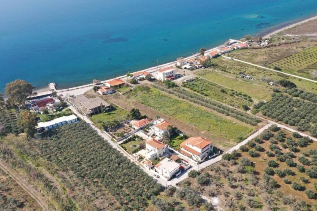 Vue aérienne d’une propriété côtière comprenant plusieurs bâtiments, notamment une grande villa avec un toit rouge, des constructions plus petites adjacentes et une plage en arrière-plan.