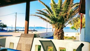 A covered outdoor seating area with a palm tree, a view of the sea, and a table with a blue surface. - V&E's Apartments (Ermionida)