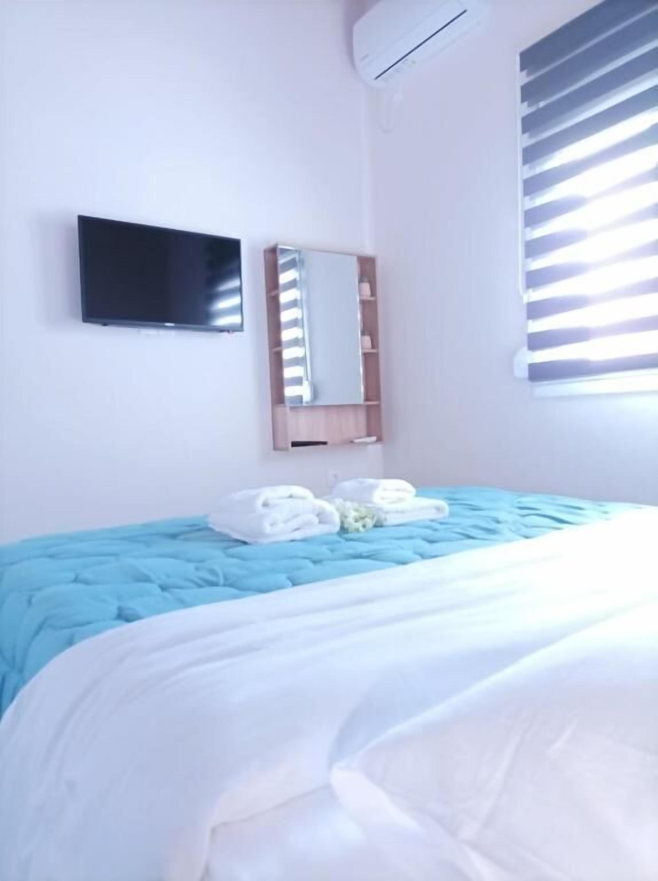 Een slaapkamer met een bed, een flatscreen televisie, een spiegel en een raam met zonwering.