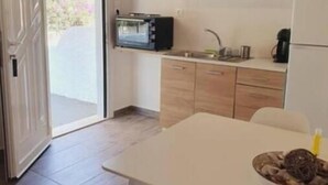 A compact kitchen with wooden cabinets, a microwave, a sink, and a dining table with chairs. - V&E's Apartments (Ermionida)
