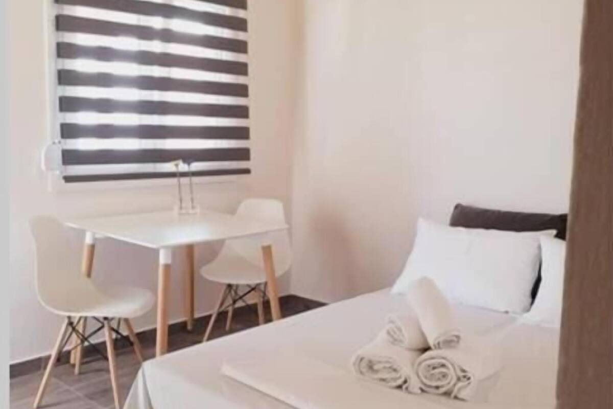 A bedroom with a bed, a desk, two chairs, and a window with blinds.