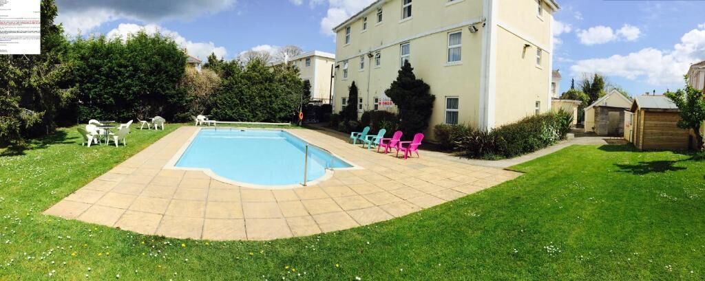 A swimming pool with lounge chairs, a grassy lawn, and a building with multiple windows.