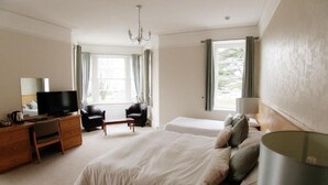 Ein Hotelzimmer mit einem großen Bett, einem Schreibtisch mit Fernseher, einem Sessel und einem Fenster mit Vorhängen.