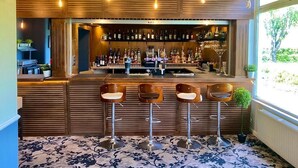 Eine Bar mit Holzwandverkleidung, einer Auswahl an Flaschen und vier Hockern.