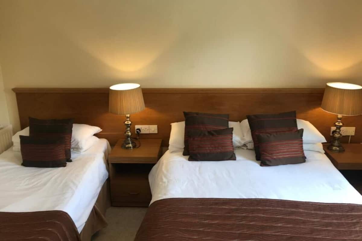 A hotel room with two single beds, each with a wooden headboard, white bedding, and brown striped pillows. There are bedside lamps on each nightstand.