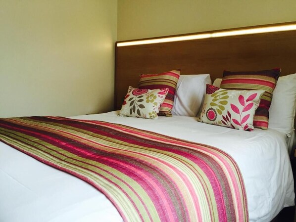 A neatly made bed with a striped blanket and floral pillows. - Anchorage Hotel & Spa (Torquay)