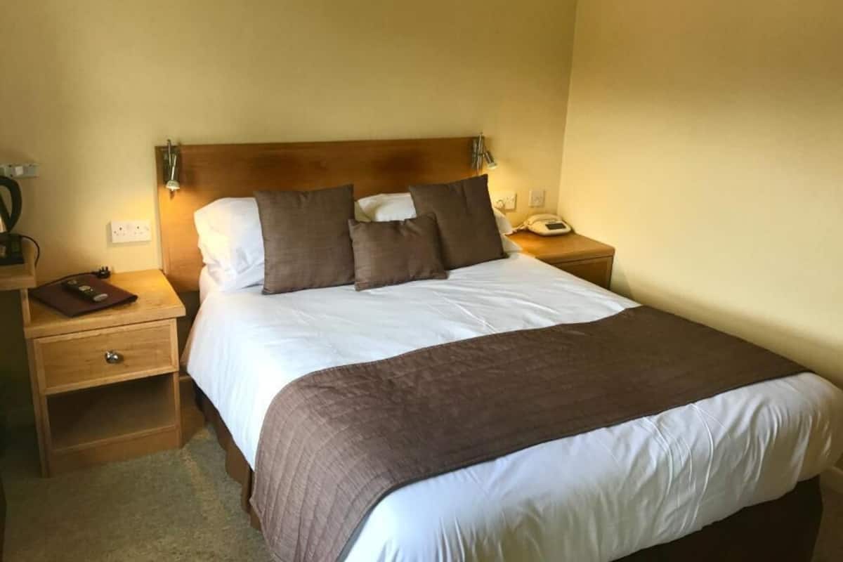 A neatly made bed with a wooden headboard, two bedside tables with lamps, and a telephone on one of the tables.