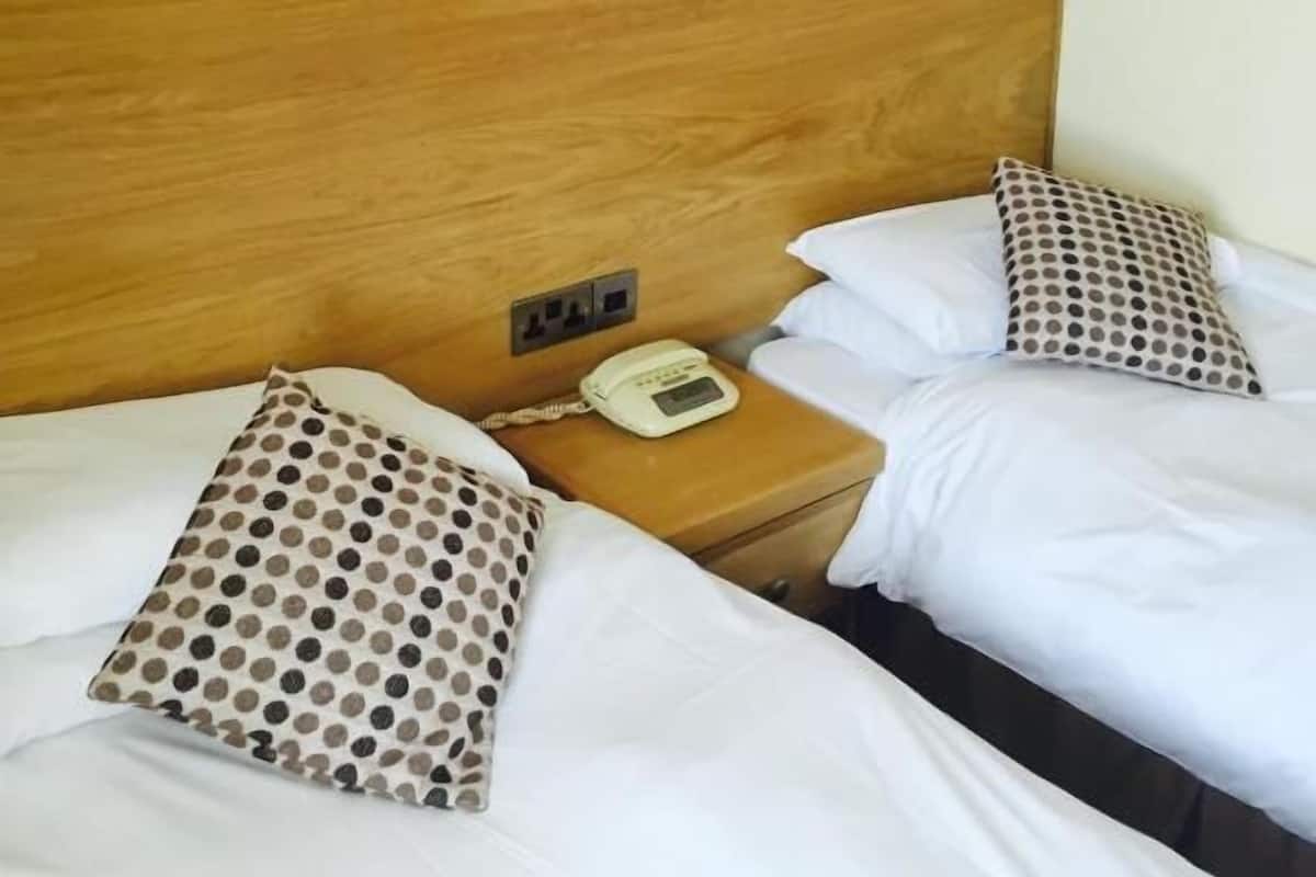 A hotel room with two beds, a wooden headboard, a nightstand with a telephone, and a black and white painting on the wall.