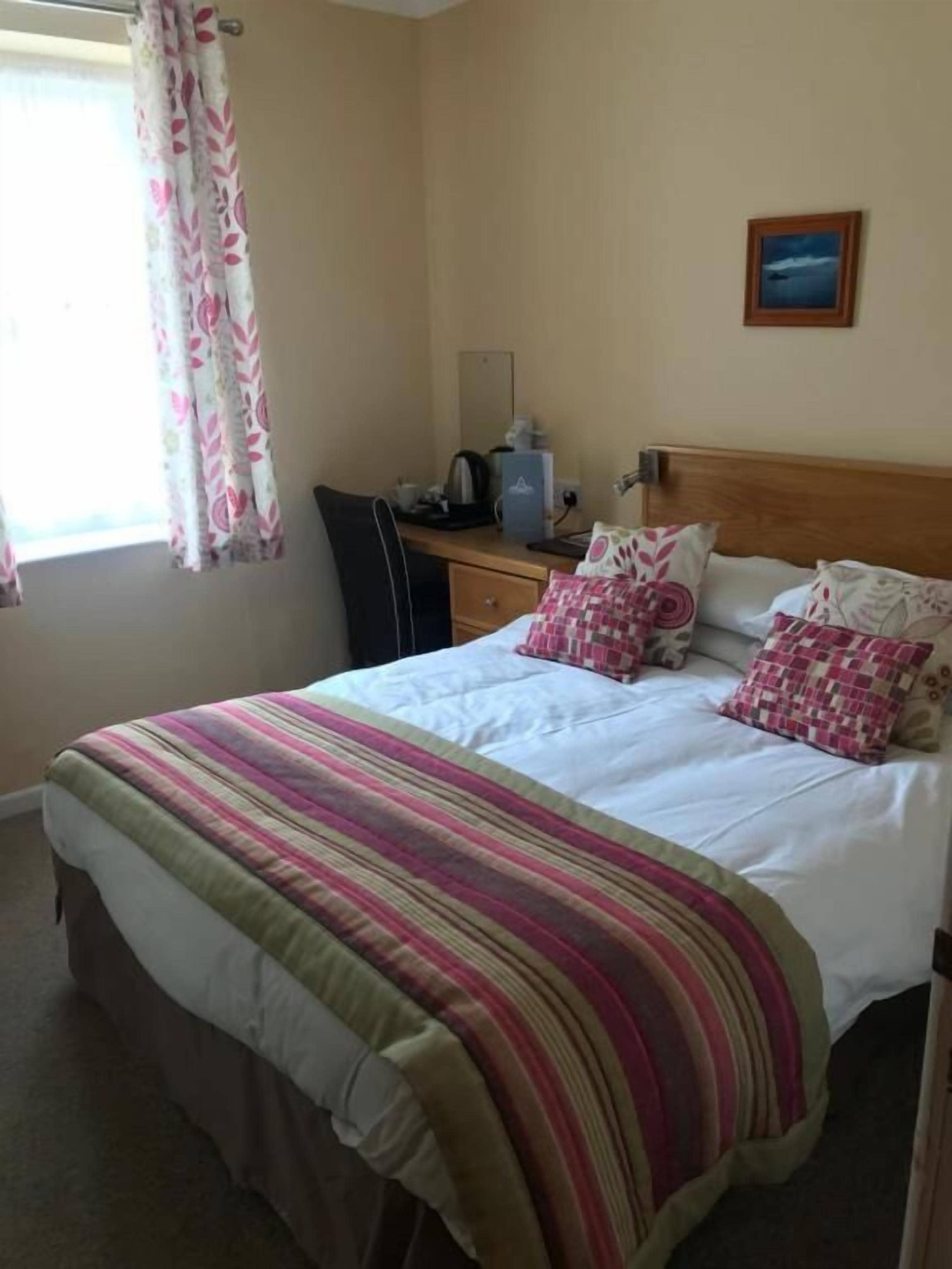 A hotel room with a bed, a desk with a computer, a chair, and a window with curtains.
